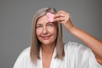 Photo of Woman massaging her face with rose quartz gua sha tool on grey background
