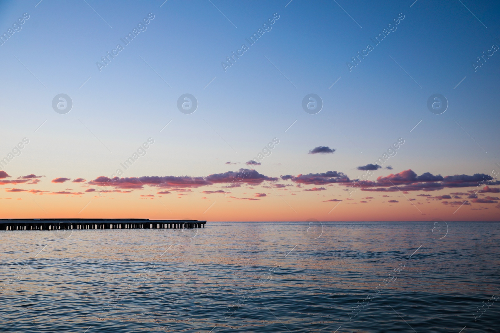 Photo of Picturesque view of pier in sea under beautiful sky at sunset