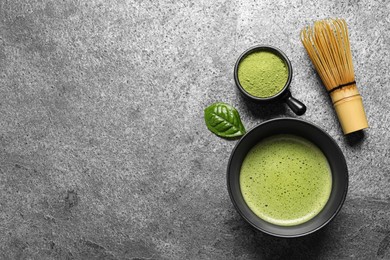 Photo of Cup of fresh matcha tea, bamboo whisk and green powder on grey table, flat lay. Space for text