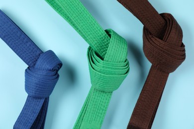 Colorful karate belts on light blue background, flat lay