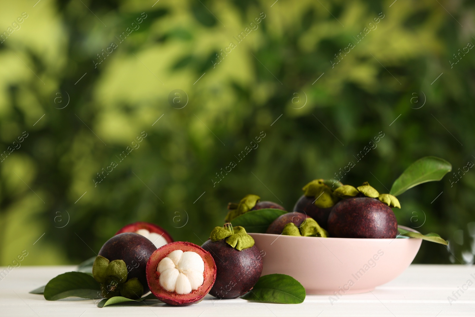 Photo of Delicious ripe mangosteen fruits on white wooden table outdoors, space for text