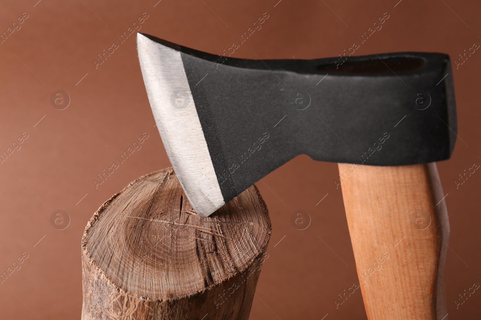 Photo of Metal axe in wooden log on brown background, closeup