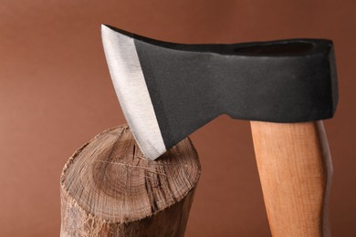 Photo of Metal axe in wooden log on brown background, closeup