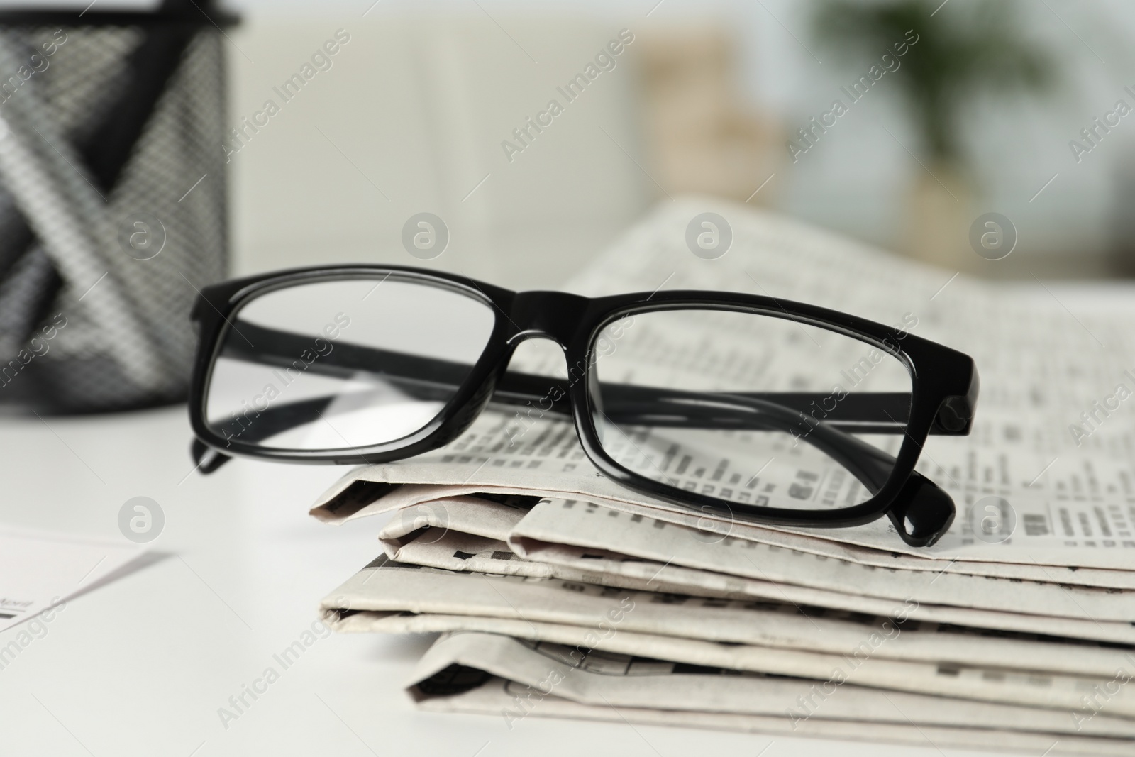 Photo of Stack of newspapers and glasses on white table indoors, closeup