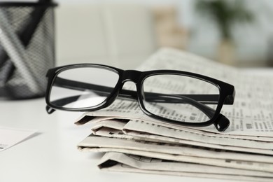 Stack of newspapers and glasses on white table indoors, closeup