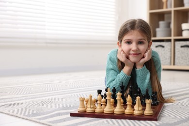 Photo of Cute girl playing chess on floor in room. Space for text
