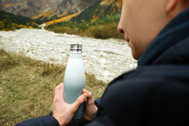 Boy holding thermo bottle with drink in mountains, closeup