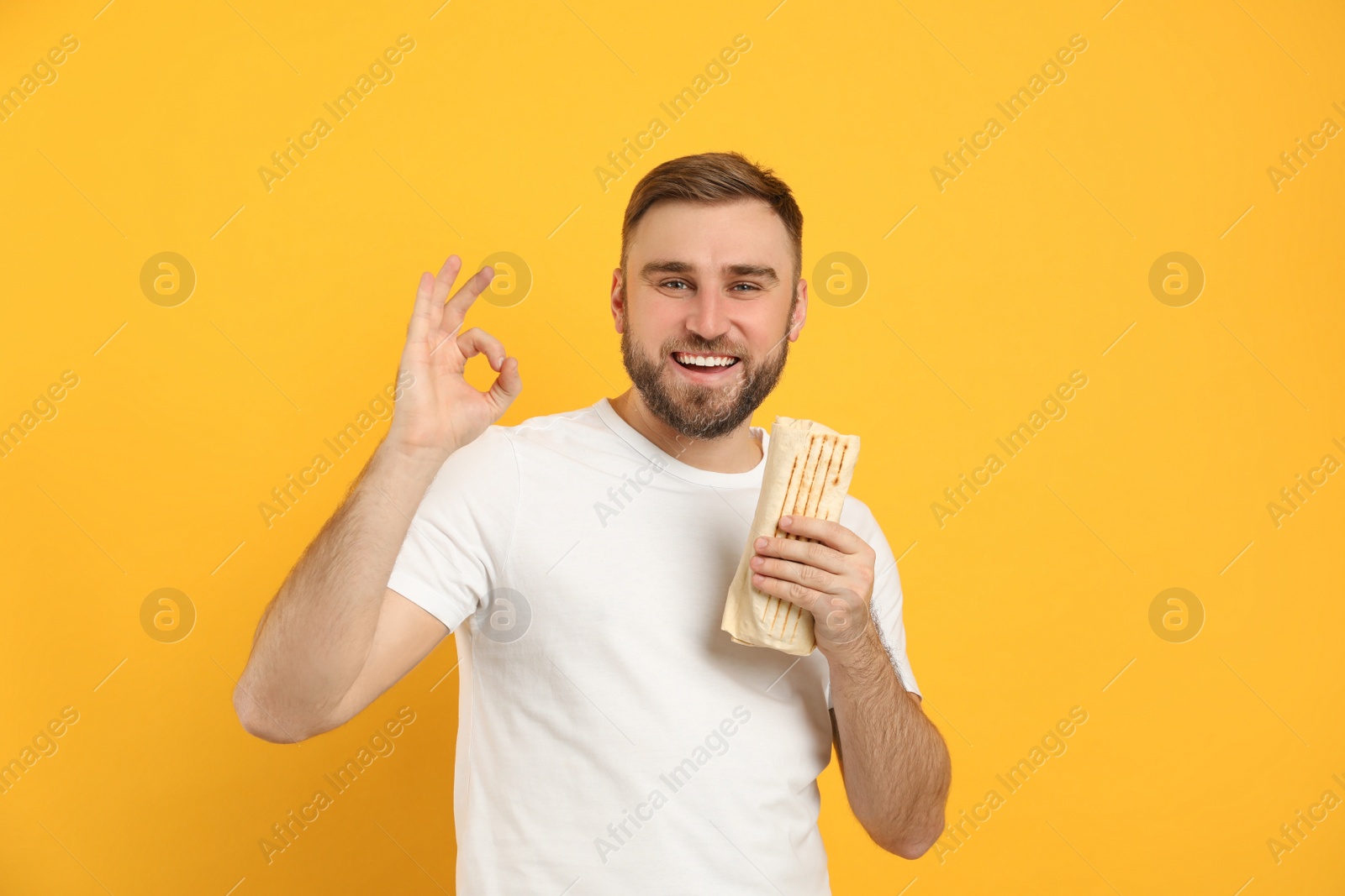 Photo of Young man with delicious shawarma on yellow background