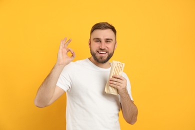Young man with delicious shawarma on yellow background