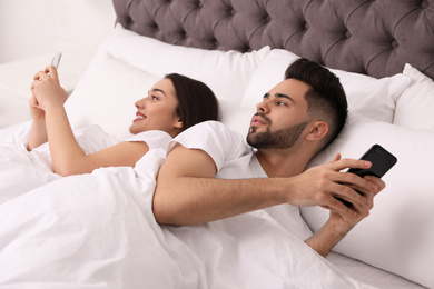 Young couple with smartphones in bed at home