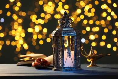 Photo of Arabic lantern, Quran, dates and Aladdin magic lamp on table against blurred lights at night