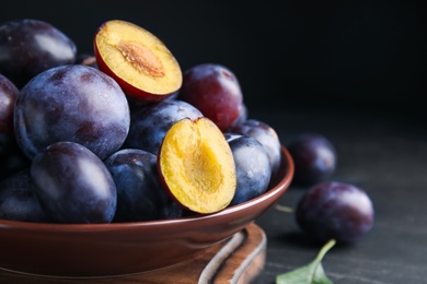 Photo of Delicious ripe plums in bowl on black table, closeup