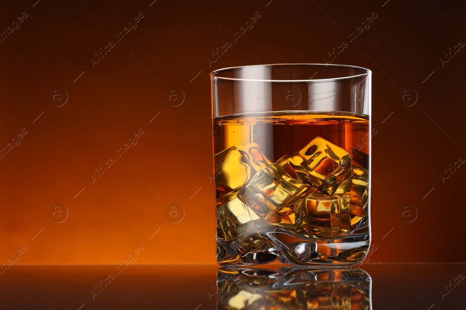 Photo of Whiskey with ice cubes in glass on color background, space for text