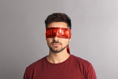 Man wearing red blindfold with word Atheism on light grey background