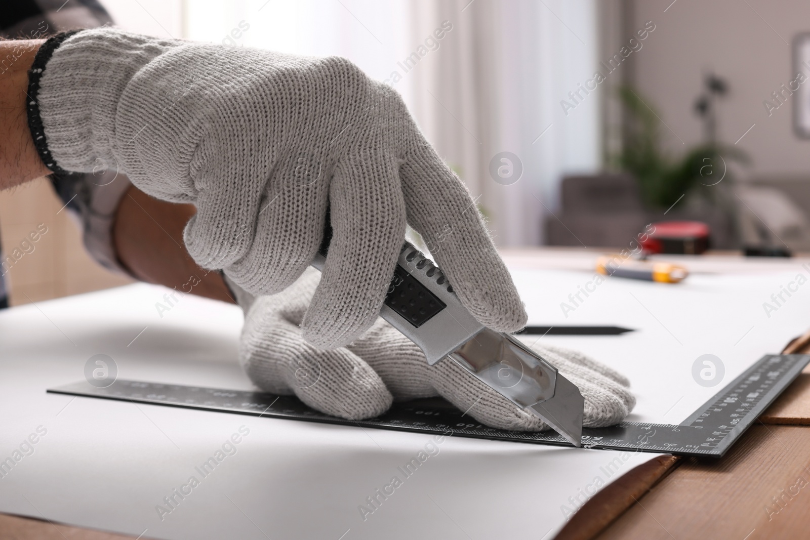 Photo of Worker cutting paper with utility knife and ruler at wooden table indoors, closeup