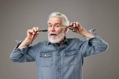 Photo of Senior man with mustache holding blade and scissors on grey background