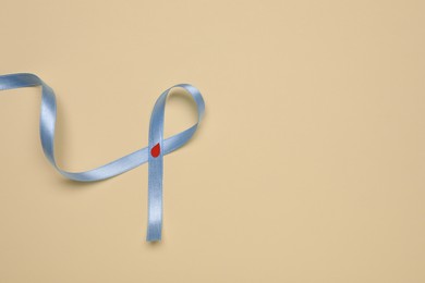 Photo of Light blue ribbon with paper blood drop on beige background, top view and space for text. Diabetes awareness