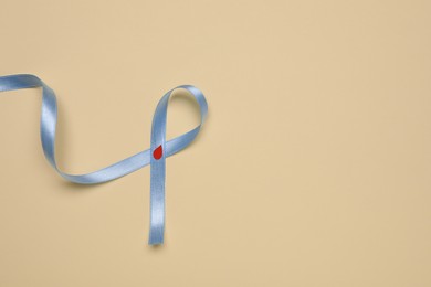 Light blue ribbon with paper blood drop on beige background, top view and space for text. Diabetes awareness