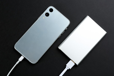 Mobile phone charging with power bank on black  background, flat lay