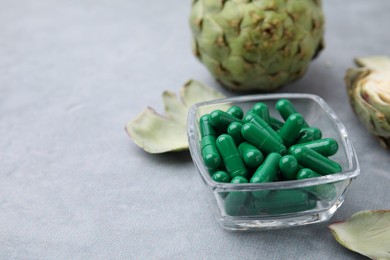 Photo of Bowl with pills and fresh artichokes on grey table, closeup. Space for text