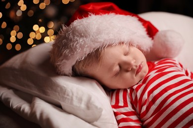 Baby in Christmas pajamas and Santa hat sleeping on bed indoors