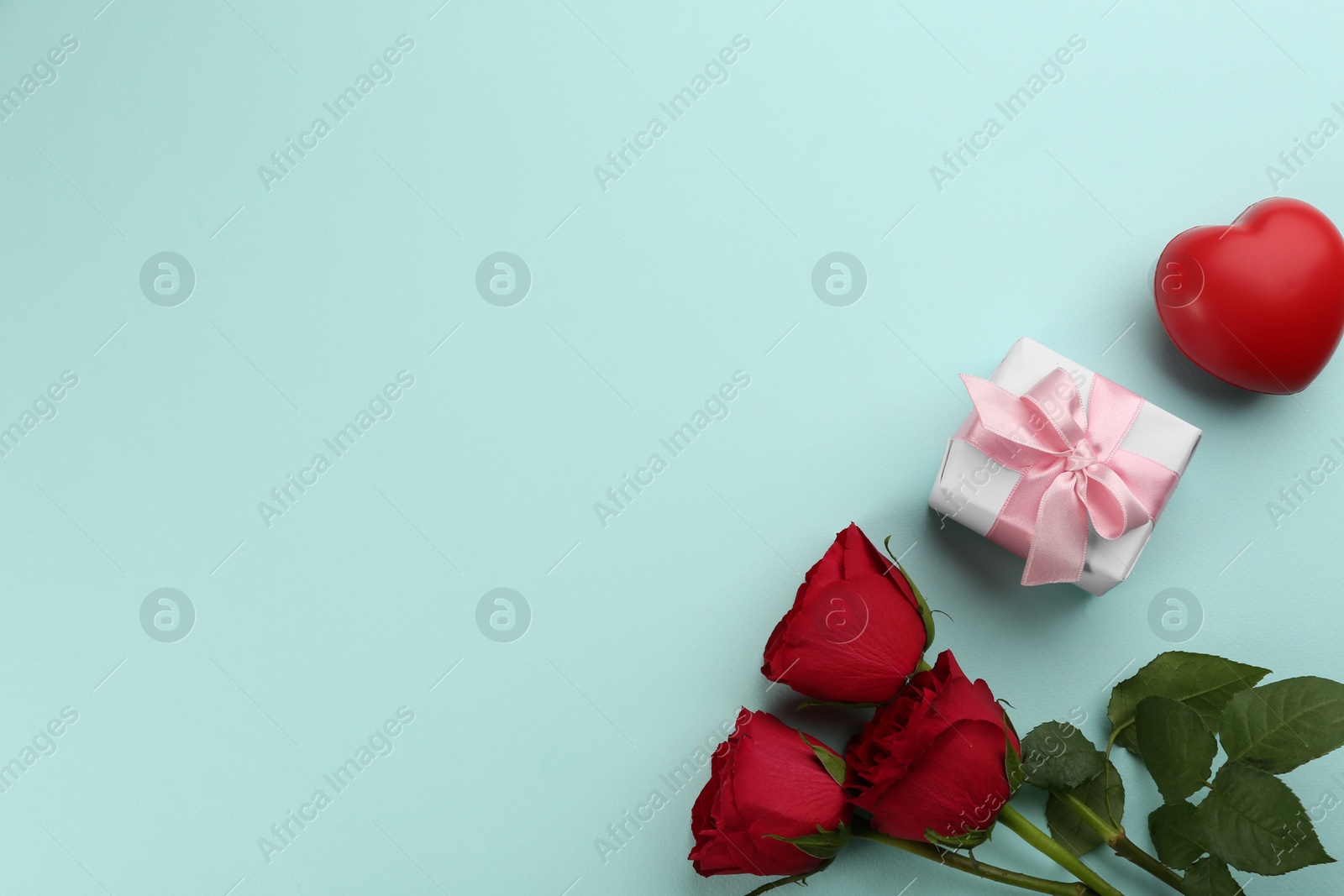 Photo of Beautiful gift box, roses and red heart on turquoise background, flat lay with space for text. Valentine's day celebration