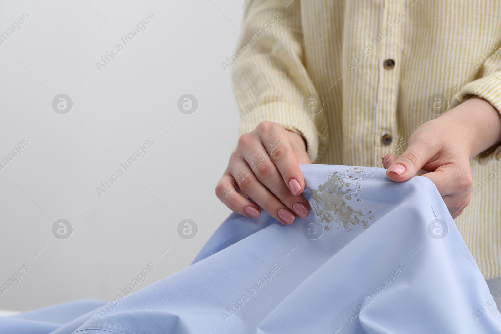 Photo of Woman holding shirt with stain against light background, closeup. Space for text