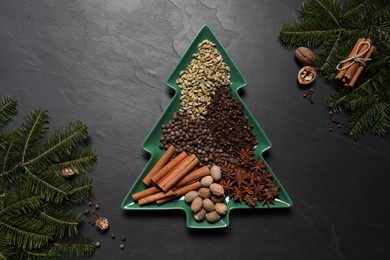 Different spices, nuts and fir branches on dark gray textured table, flat lay