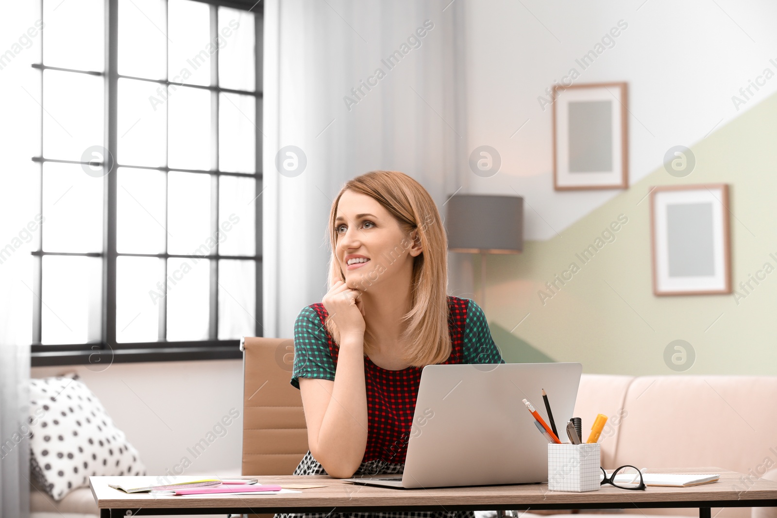 Photo of Young woman working with laptop at desk in home office