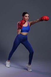 Photo of Beautiful woman wearing boxing gloves training in color lights on grey background