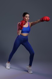 Beautiful woman wearing boxing gloves training in color lights on grey background