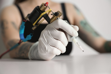 Tattoo artist with professional machine at table against light background, closeup