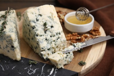 Photo of Tasty blue cheese with thyme, honey and walnuts on wooden board, closeup