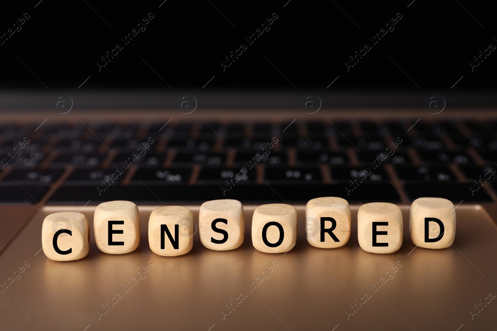 Photo of Wooden cubes with word Censored on laptop, closeup. Space for text