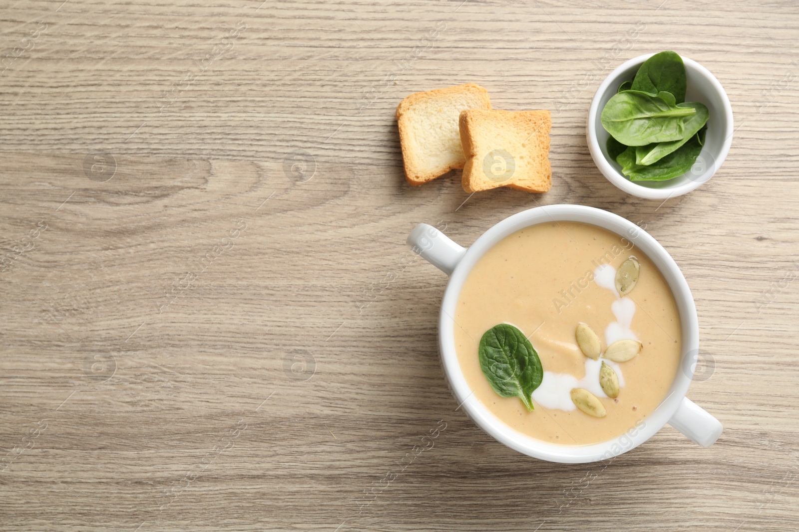 Photo of Healthy cream soup high in vegetable fats, bread and spinach on wooden table, flat lay. Space for text