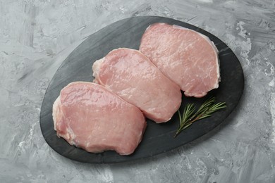 Photo of Pieces of raw pork meat and rosemary on grey textured table, top view