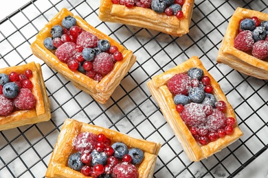 Photo of Cooling rack and fresh delicious puff pastry with sweet berries on white marble table, flat lay