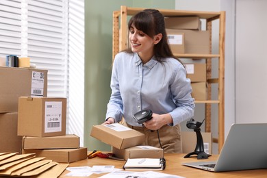 Photo of Parcel packing. Post office worker with scanner reading barcode at wooden table indoors