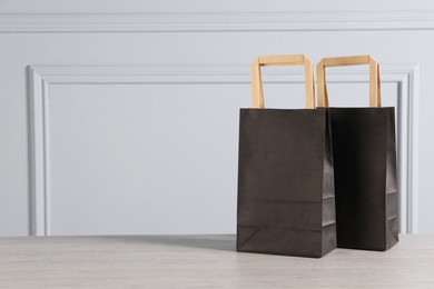 Photo of Black paper bags on wooden table against light grey wall, space for text