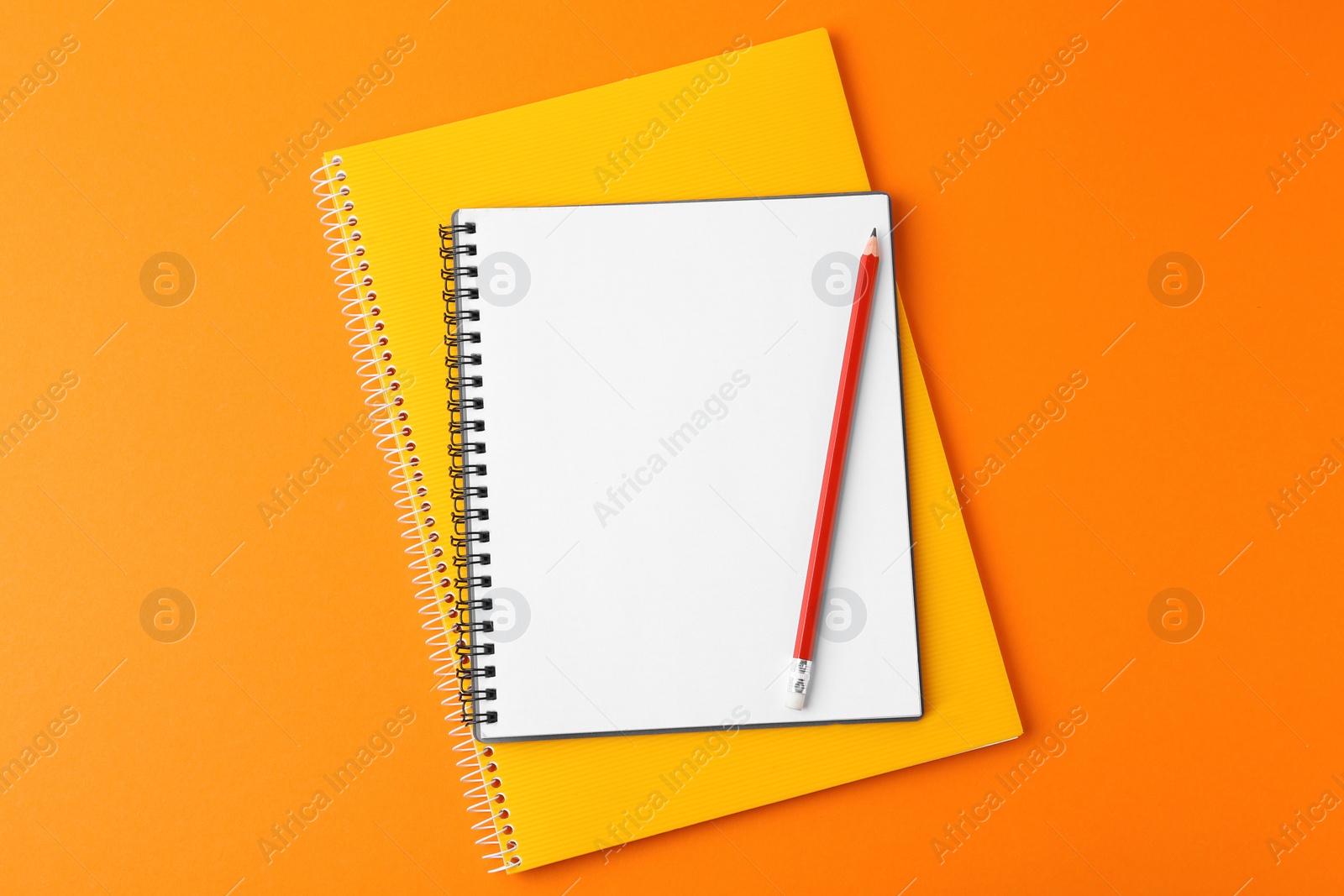 Photo of Notebooks with pencil on orange background, top view