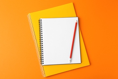 Photo of Notebooks with pencil on orange background, top view