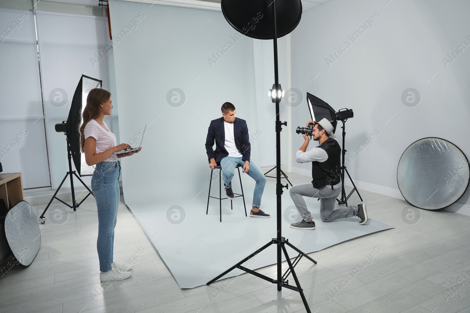 Photo of Professional photographer with assistant taking picture of young man in modern studio