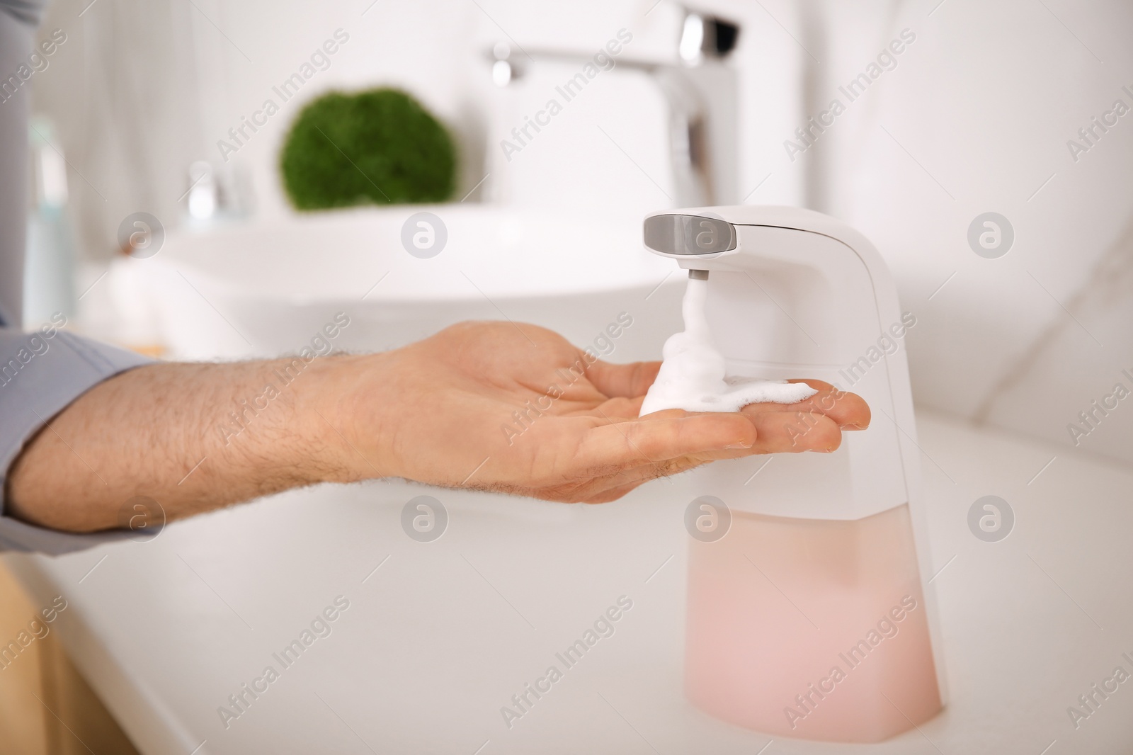 Photo of Man using automatic soap dispenser in bathroom, closeup