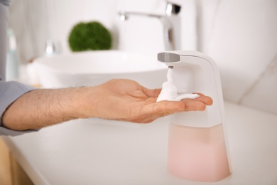 Man using automatic soap dispenser in bathroom, closeup