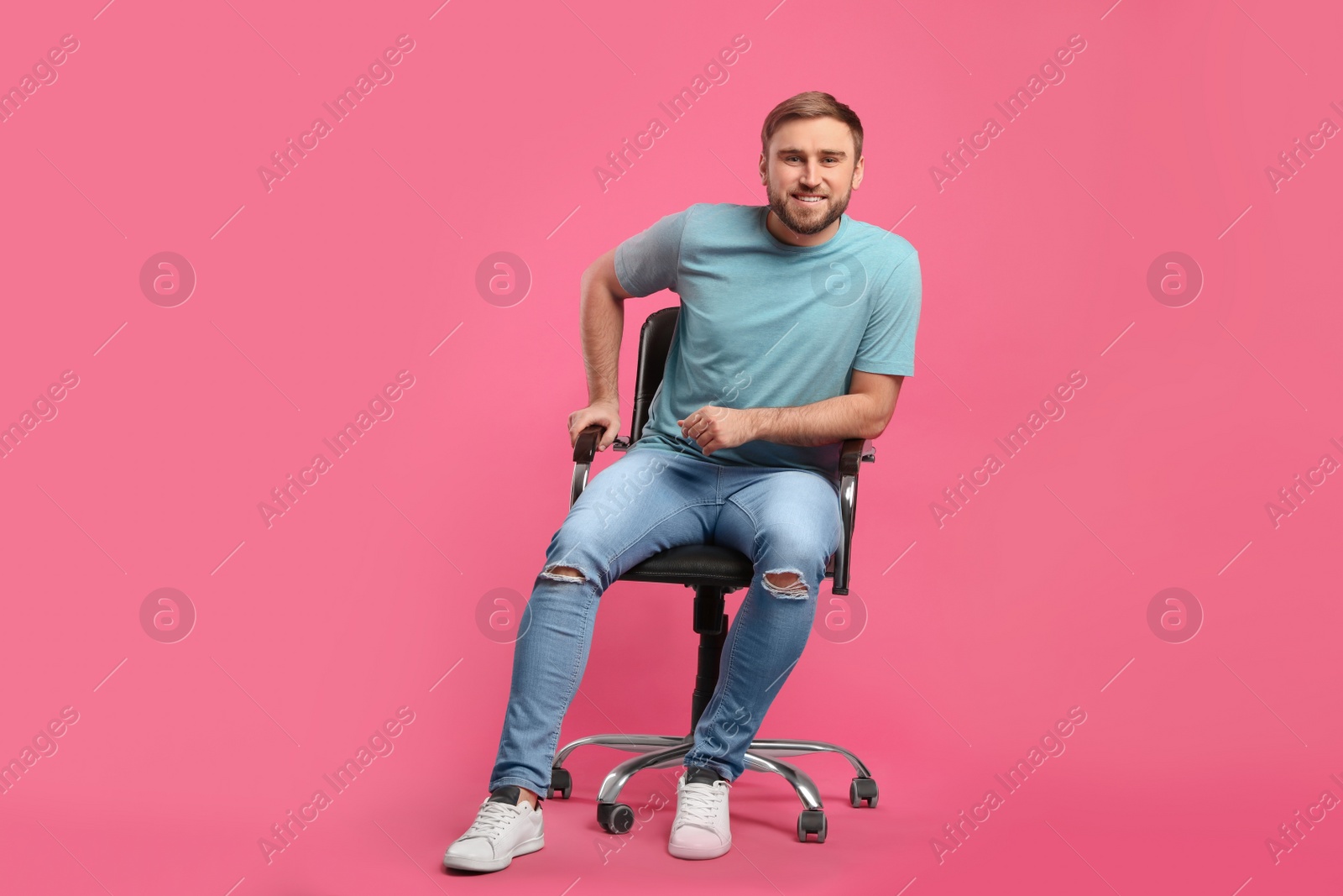 Photo of Young man sitting in comfortable office chair on pink background
