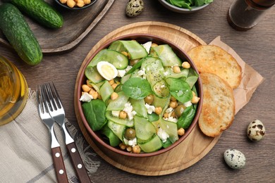 Photo of Delicious cucumber salad and toasted bread served on wooden table, flat lay