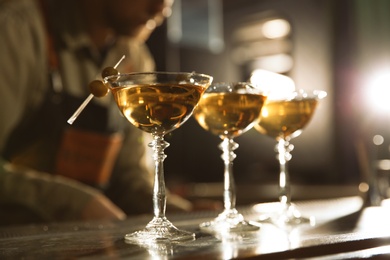 Photo of Glasses of martini cocktail with olives on bar counter. Space for text