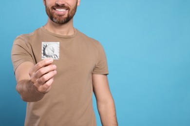 Man holding condom on light blue background, closeup and space for text. Safe sex
