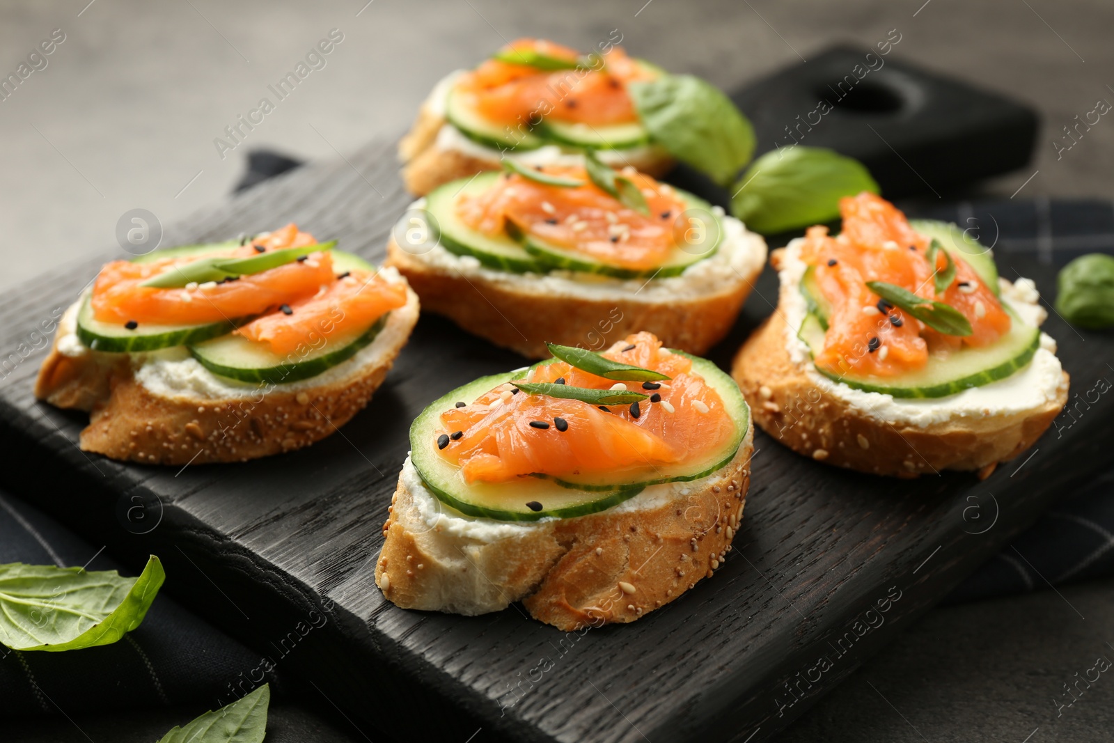 Photo of Tasty canapes with salmon, cucumber and cream cheese on grey table, closeup