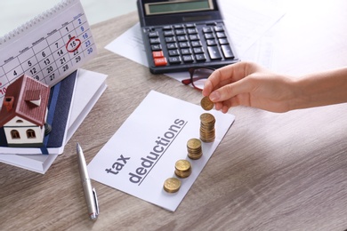 Woman stacking coins on paper with phrase TAX DEDUCTIONS at table